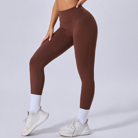 Frau in brauner Sportleggings und weißen Sneakers, seitlich stehend. Fitnessmode, bequeme Leggings, Sportbekleidung für Damen.