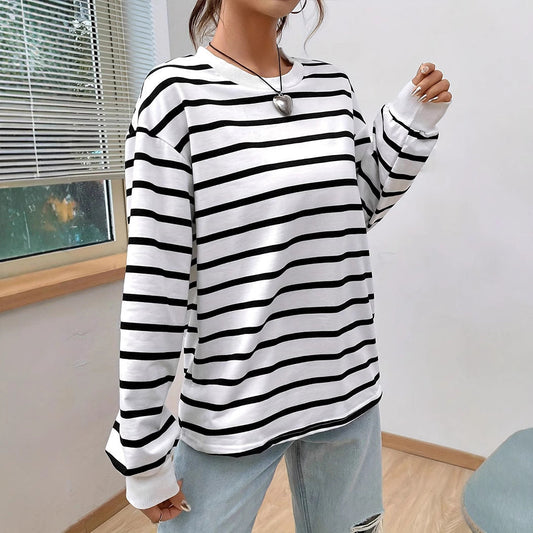 Frau trägt gestreiftes Langarmshirt, schwarz-weiß, lässig, modisch, mit Herzanhänger, vor Fenster. Perfekt für Freizeitmode und Streetstyle.