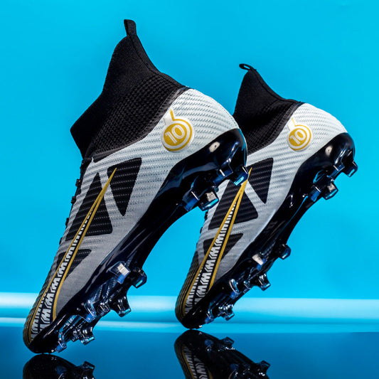 Zwei moderne Fußballschuhe mit Stollen, schwarz-weiß mit goldenen Akzenten, vor blauem Hintergrund. Ideal für Rasenplätze, sportliches Design.