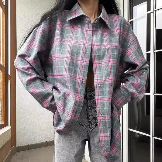 Frau in kariertem Hemd, graue und rosa Töne, kombiniert mit grauen Jeans, steht auf einem Balkon. Modetrend, lässiger Stil, Herbstmode.
