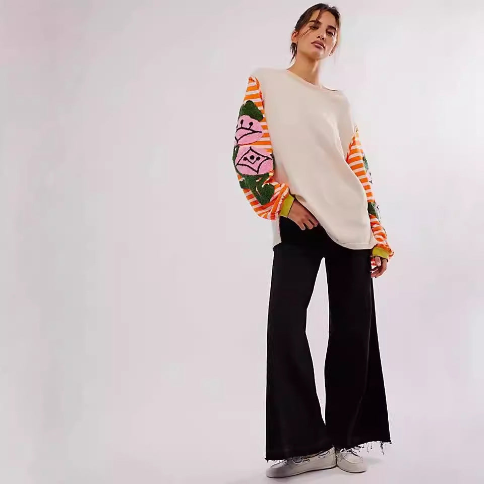Frau in modischem Outfit mit buntem Pullover und schwarzen Schlaghosen, lässiger Look, trendige Damenmode, urbaner Stil, weiße Sneakers.