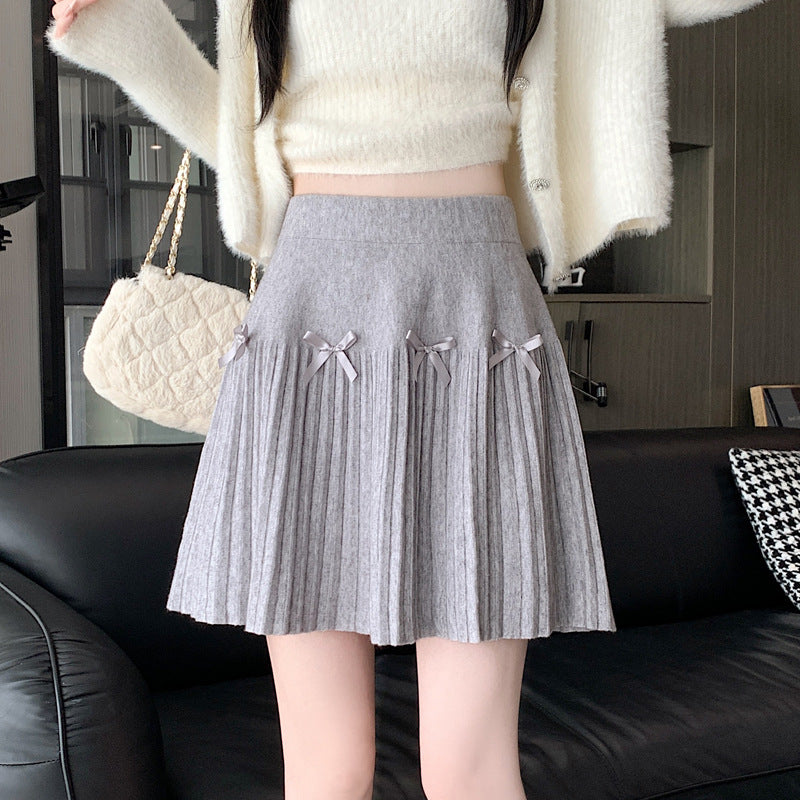 Frau in weißem Pullover und grauem Faltenrock mit Schleifen, hält eine beige Handtasche. Modetrend, eleganter Look, Herbstmode.