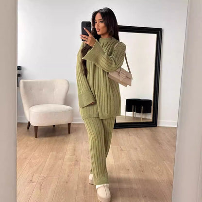 Frau in grünem Strickpullover und Hose, posiert vor Spiegel, hält Smartphone. Modernes Wohnzimmer, beiger Sessel, Holzfußboden. Fashion, Selfie.