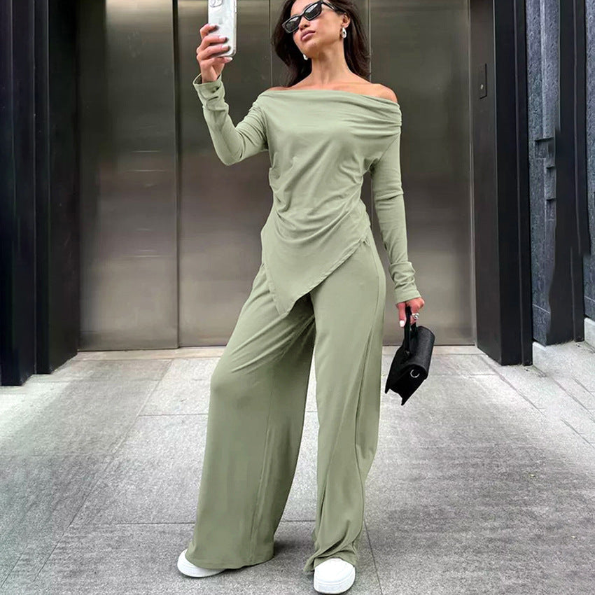 Frau in grünem Off-Shoulder-Jumpsuit macht Selfie, trägt Sonnenbrille und weiße Sneaker, steht vor modernem Gebäude. Fashion, Streetstyle, Mode.