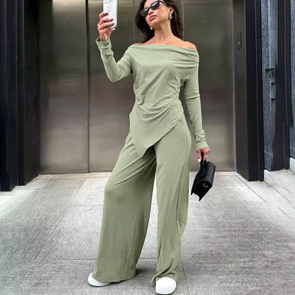 Frau in grünem Off-Shoulder-Jumpsuit macht Selfie, trägt Sonnenbrille und weiße Sneaker, steht vor modernem Gebäude. Fashion, Streetstyle, Mode.