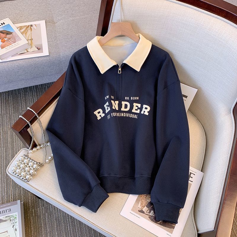 Dunkelblauer Pullover mit weißem Kragen und Reißverschluss, Aufschrift "RENDER", auf einem Sessel liegend, neben einer Perlenhandtasche.
