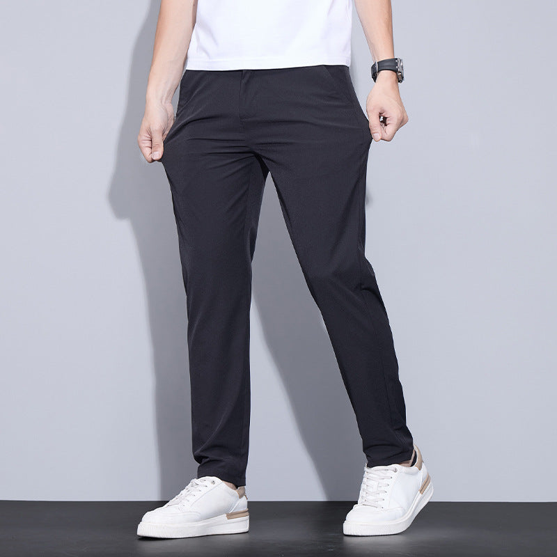 Mann in schwarzer Hose und weißen Sneakers vor grauem Hintergrund. Moderne Herrenmode, lässiger Stil, bequeme Freizeitkleidung.