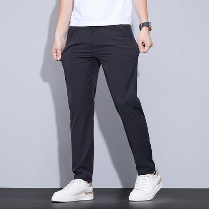 Mann in schwarzer Hose und weißen Sneakers vor grauem Hintergrund. Moderne Herrenmode, lässiger Stil, bequeme Freizeitkleidung.