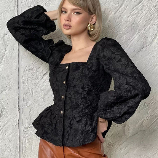 Frau in schwarzer, strukturierter Bluse mit Puffärmeln und brauner Hose vor weißer Wand. Modetrend, elegante Damenmode, Herbstoutfit.