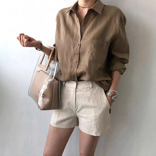 Frau in brauner Leinenbluse und beigen Shorts, hält transparente Handtasche. Modetrend, Sommeroutfit, lässiger Stil.