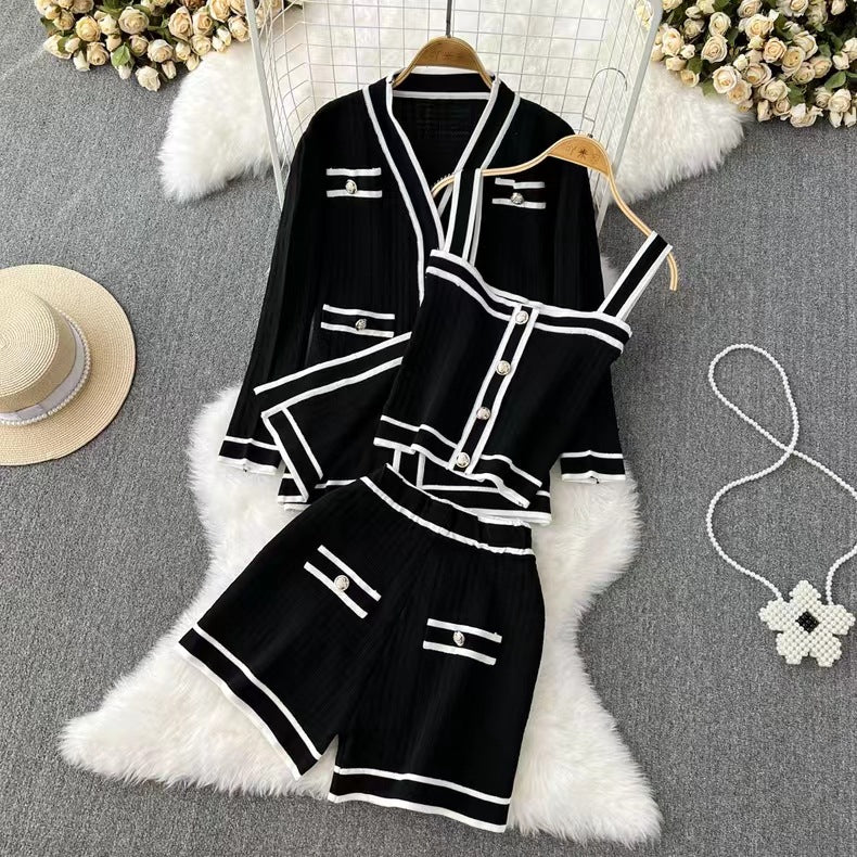 Schwarzes Damen-Zweiteiler-Set mit weißen Streifen, bestehend aus Blazer, Top und Shorts, auf weißem Fellteppich, umgeben von Blumen.