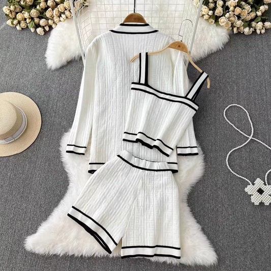Weiße Damen-Pyjama-Set mit schwarzem Rand, bestehend aus Hemd, Shorts und Top, auf grauem Teppich mit Blumen und Strohhut. Luxuriöse Nachtwäsche.