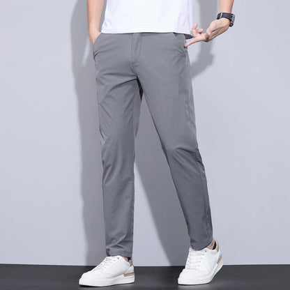 Mann trägt graue Chinohose und weiße Sneaker vor grauem Hintergrund. Modische Herrenbekleidung, lässiger Stil, moderne Freizeitmode.
