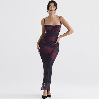 Frau in elegantem, langem, schwarzem Kleid mit roten Blumenmustern, Spaghettiträgern und transparentem Saum, posiert vor weißem Hintergrund.