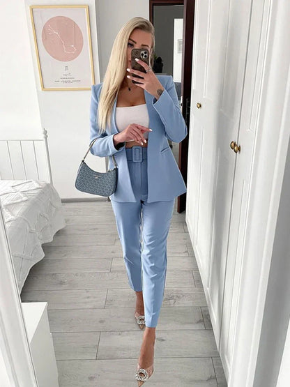 Blonde Frau im blauen Anzug macht Selfie im Spiegel. Eleganter Business-Look mit weißem Top, modischer Handtasche und Absatzschuhen.
