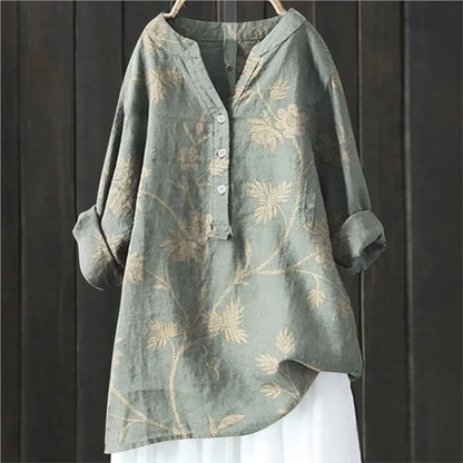 Graues Leinenhemd mit Blumenmuster, langen Ärmeln und Knopfleiste, hängend vor dunklem Holzhintergrund. Elegante Damenmode, lässiger Stil.