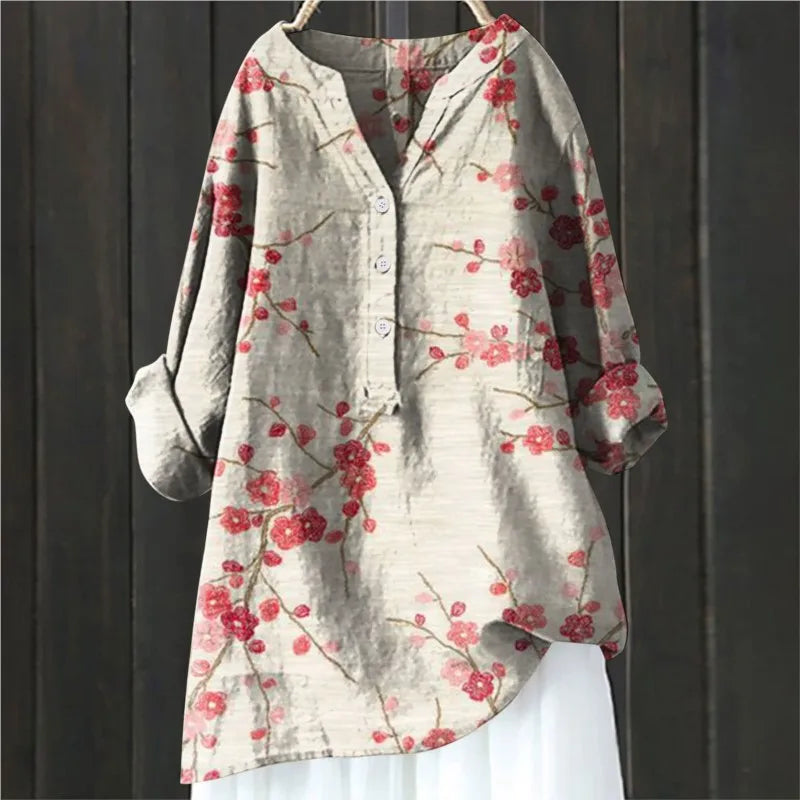 Beige Damenbluse mit roten Blumenmuster, Knopfleiste und langen Ärmeln, hängend vor dunklem Holzhintergrund. Modetrend, Frühlingsmode, Damenbekleidung.