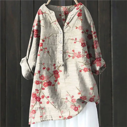 Beige Damenbluse mit roten Blumenmuster, Knopfleiste und langen Ärmeln, hängend vor dunklem Holzhintergrund. Modetrend, Frühlingsmode, Damenbekleidung.