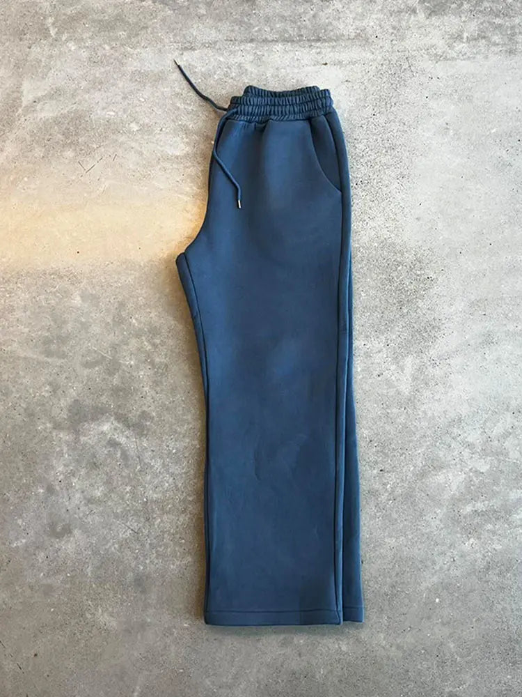 Blaue Jogginghose auf grauem Betonboden, elastischer Bund mit Kordelzug, sportlich und bequem, ideal für Freizeit und Fitness.