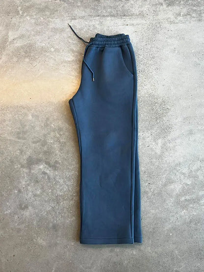 Blaue Jogginghose auf grauem Betonboden, elastischer Bund mit Kordelzug, sportlich und bequem, ideal für Freizeit und Fitness.