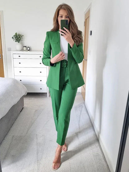 Frau im grünen Anzug macht Selfie im Schlafzimmer, moderne Einrichtung, weiße Kommode, Spiegel, modische Business-Kleidung, stilvoller Look.