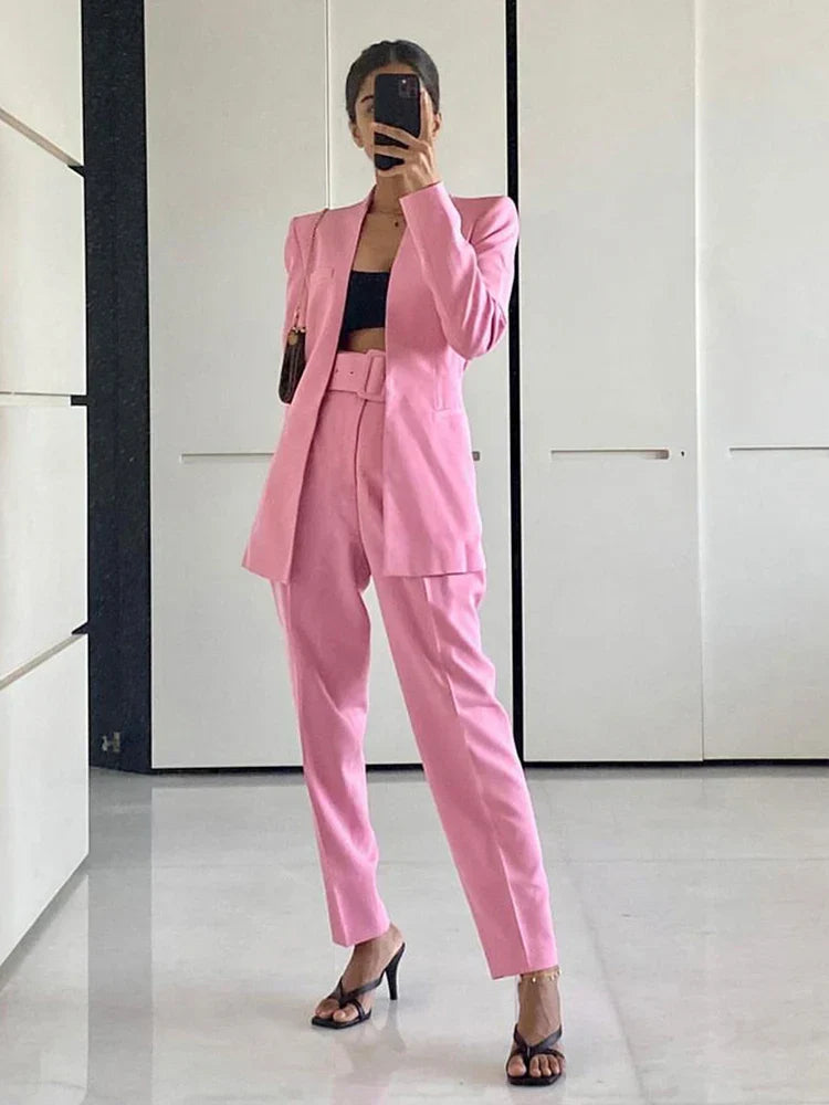 Frau in rosa Anzug mit schwarzem Top und High Heels, steht in modernem Raum. Elegante Damenmode, Business-Look, stilvolle Kleidung.