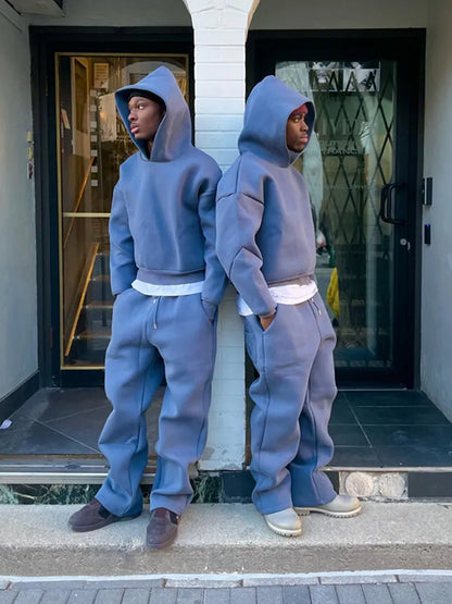 Zwei Personen in blauen Oversize-Hoodies und Jogginghosen stehen Rücken an Rücken vor einem Gebäude. Streetwear, Mode, urbaner Stil.