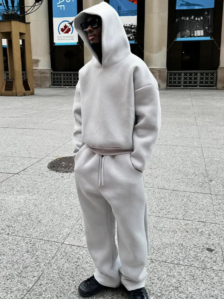 Grauer Oversize-Hoodie und Jogginghose, getragen von einer Person mit Sonnenbrille auf städtischem Platz. Streetwear, lässiger Stil, Mode.