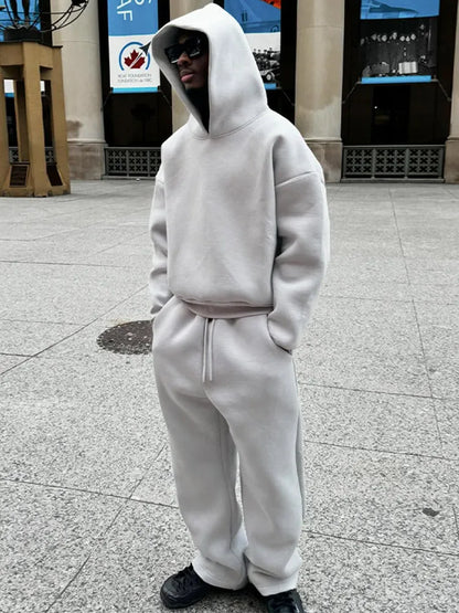 Grauer Oversize-Hoodie und Jogginghose, getragen von einer Person mit Sonnenbrille auf städtischem Platz. Streetwear, lässiger Stil, Mode.