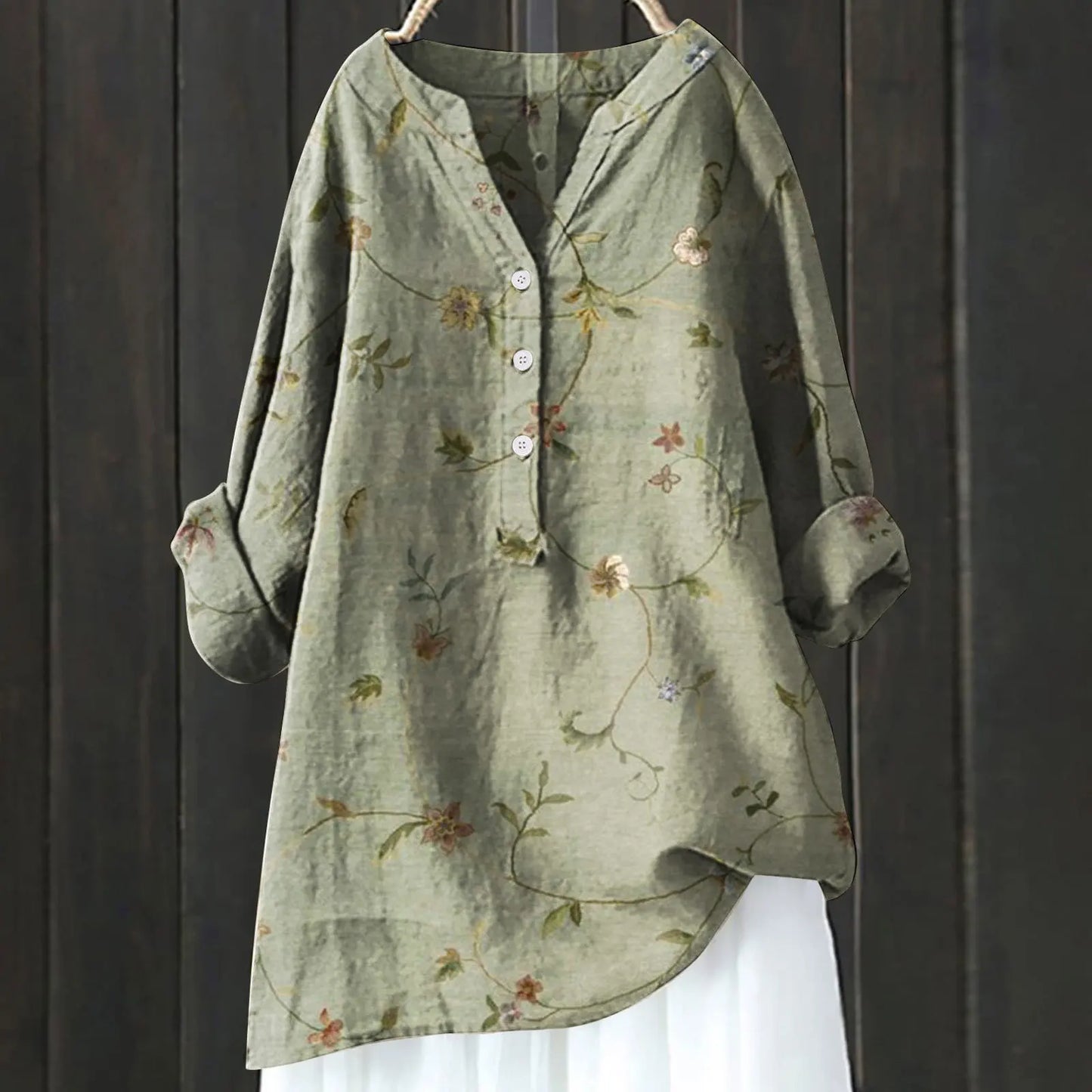 Grüne Leinenbluse mit Blumenmuster, Knopfleiste und langen Ärmeln vor dunklem Holzhintergrund. Damenmode, lässiger Stil, Herbstkleidung.
