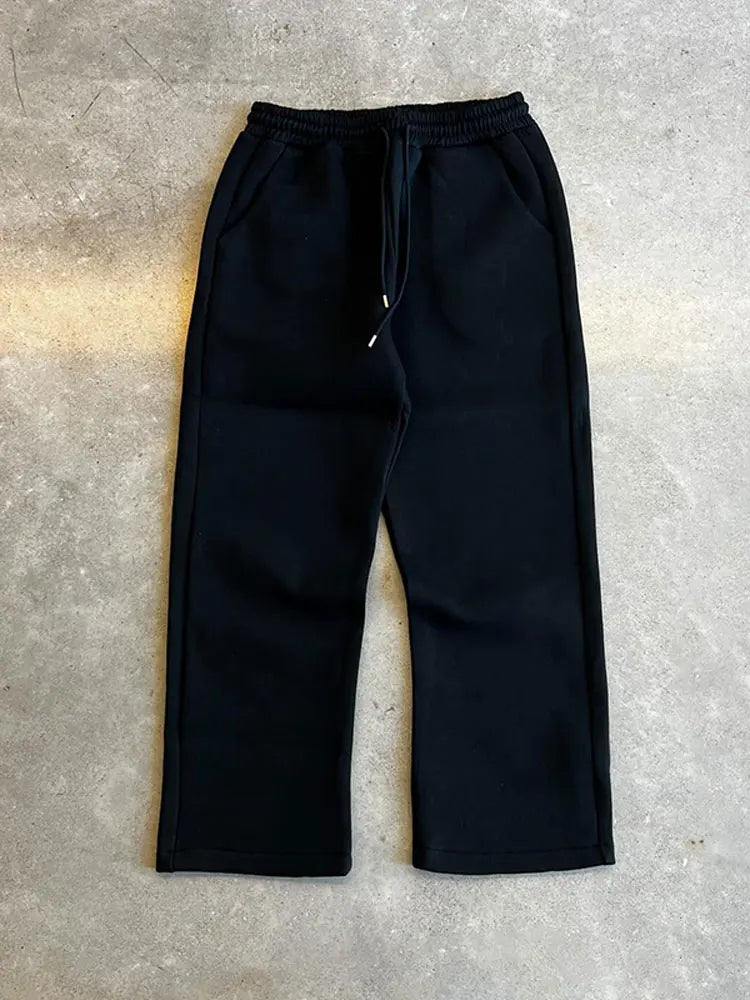 Schwarze Jogginghose aus Baumwolle auf grauem Hintergrund, elastischer Bund mit Kordelzug, seitliche Taschen, bequeme Freizeitmode.