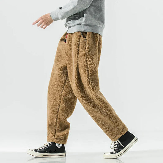 Person trägt braune Fleece-Jogginghose und schwarze Converse-Sneaker. Bequeme, warme Wintermode für Herren. Lässiger Stil, ideal für kalte Tage.