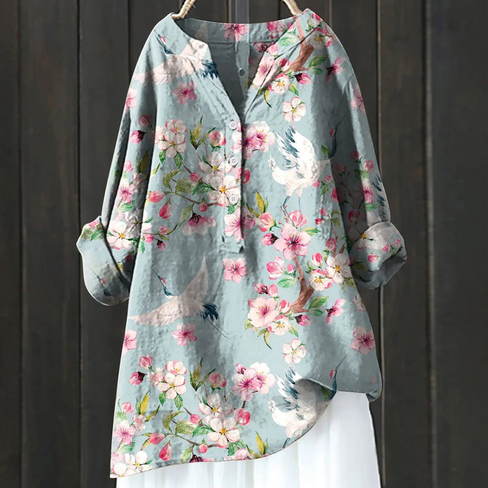 Blaues Damenhemd mit Blumen- und Vogelmuster, Langarm, lockerer Schnitt, hängend vor dunklem Holzhintergrund. Modetrend, Frühlingsmode.