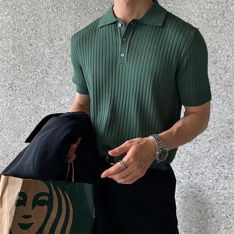 Mann in grünem Polohemd mit geripptem Muster hält eine Starbucks-Tüte und eine schwarze Jacke. Eleganter Stil, Freizeitmode, Accessoires.