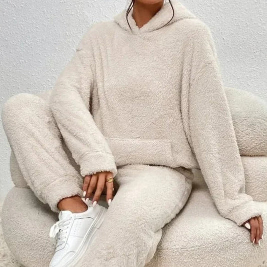 Frau in beigem, flauschigem Hoodie und Jogginghose sitzt auf einem Sessel. Bequeme Loungewear, gemütlicher Look, modische Freizeitkleidung.
