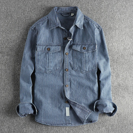 Gestreiftes Jeanshemd mit langen Ärmeln, zwei Brusttaschen und Knopfleiste, auf grauem Hintergrund. Modisches Herrenhemd, lässiger Stil.