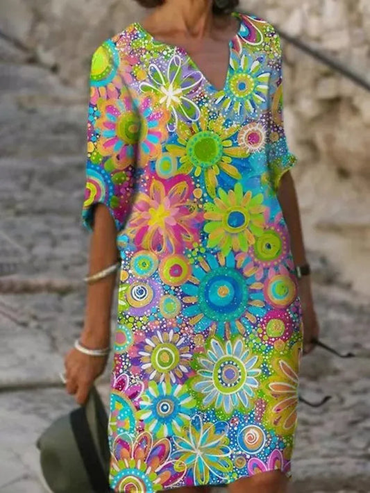 Frau in buntem, geblümtem Sommerkleid mit leuchtenden Farben und Blumenmuster, steht auf einem gepflasterten Weg. Perfekt für Sommermode und Freizeit.