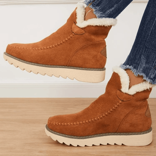 Braune Damen-Winterstiefel aus Wildleder mit weißem Kunstfellfutter, dicker Sohle und Ziernähten, getragen mit blauen Jeans.