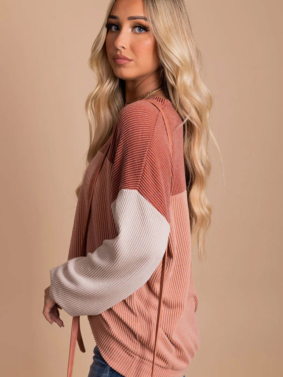 Blonde Frau in modischem, gestreiftem Pullover in Rosa- und Beigetönen vor beigem Hintergrund. Trendige Damenmode, Herbstkollektion, lässiger Stil.
