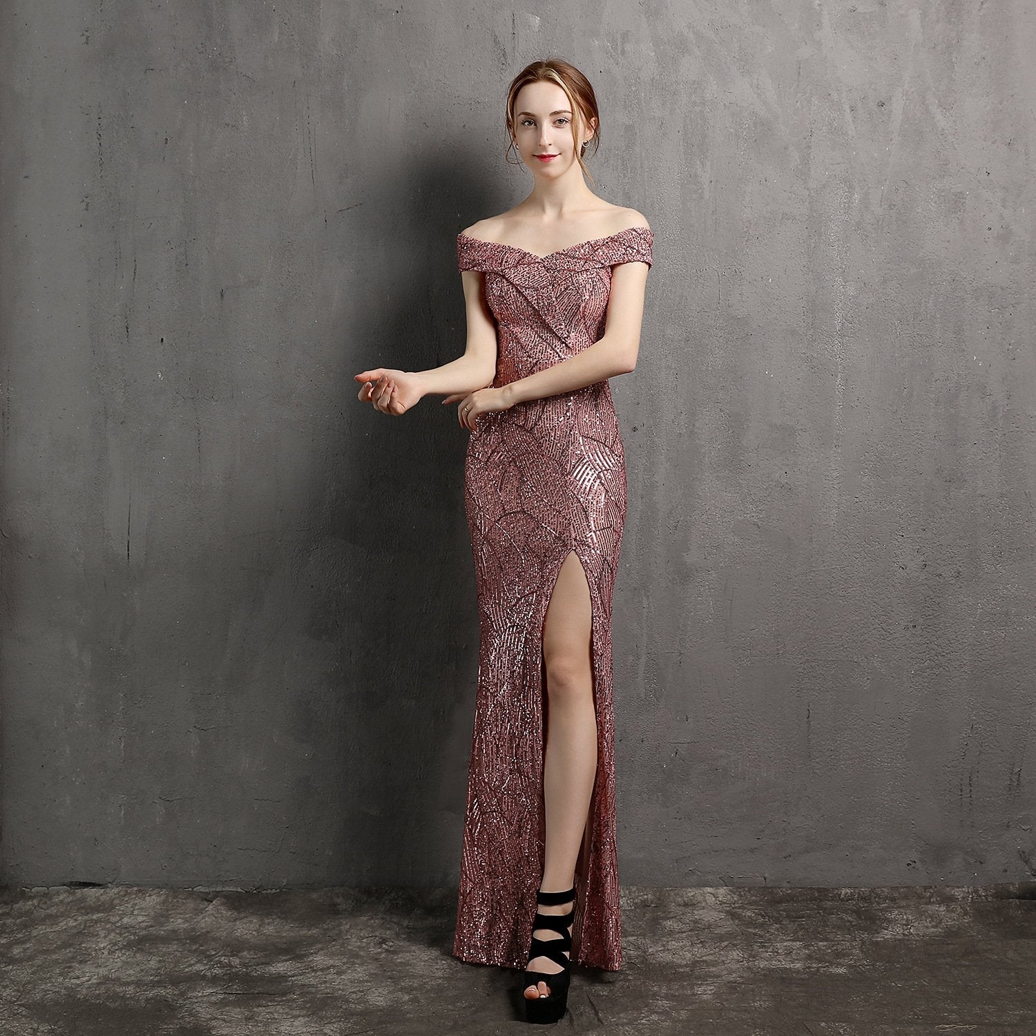 Frau in eleganter, schulterfreier Abendkleid mit Pailletten und hohem Schlitz, posiert vor grauer Wand. Perfekt für Gala oder Abendveranstaltung.