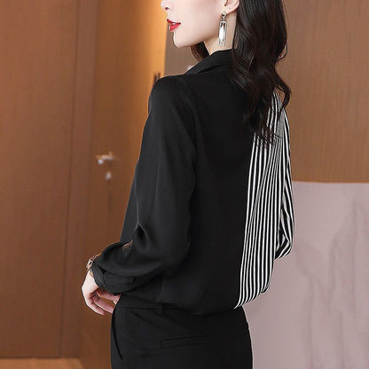 Frau in eleganter schwarzer Bluse mit gestreiftem Rückenteil, moderne Ohrringe, stilvolle Mode, Büro-Outfit, seitliche Ansicht.