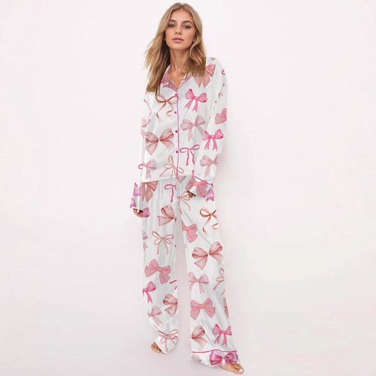 Frau in weißem Pyjama mit rosa Schleifenmuster, langärmliges Oberteil und lange Hose, modische Nachtwäsche, gemütlicher Schlafanzug.