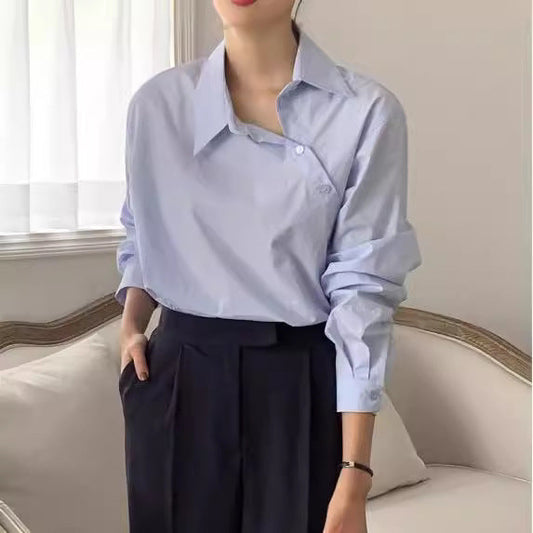 Frau in hellblauer Bluse und schwarzer Hose sitzt auf einem Sofa. Elegante, minimalistische Mode, Business-Look, stilvolle Damenbekleidung.