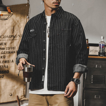 Mann in gestreifter schwarzer Jacke, weißem T-Shirt, hält Metallbecher. Lässige Mode, urbaner Stil, Vintage-Dekor im Hintergrund.