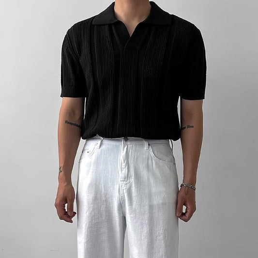 Mann trägt schwarzes Polohemd und weiße Hose vor grauem Hintergrund. Modetrend, Herrenbekleidung, eleganter Stil, minimalistisches Design.
