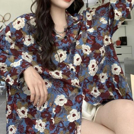 Frau in geblümter Bluse, blau-rot-weißes Muster, sitzt entspannt. Modetrend, lässiger Stil, florales Design, Freizeitkleidung.