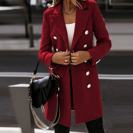 Frau in rotem Mantel mit doppelter Knopfleiste, weißem Oberteil und schwarzer Tasche. Elegante Herbstmode, stilvoller Look, urbane Kulisse.