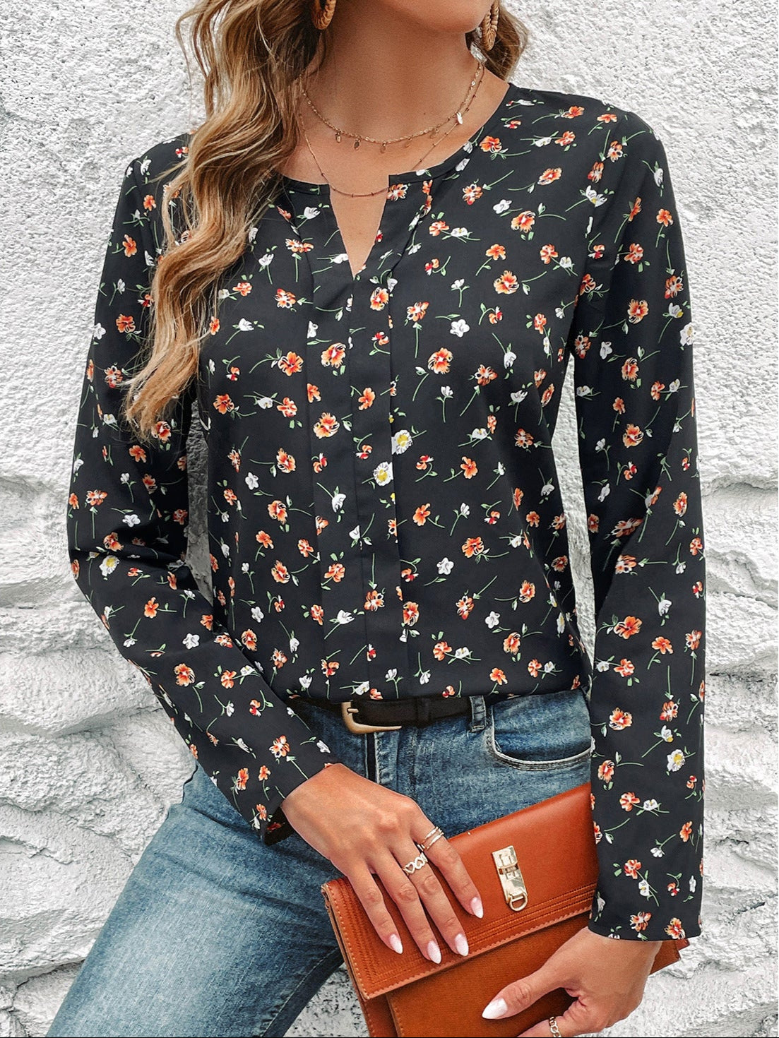 Frau in schwarzer Bluse mit Blumenmuster, blaue Jeans, braune Lederhandtasche, vor weißer Wand. Modetrend, Damenmode, Freizeitlook.