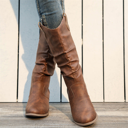 Braune Cowboystiefel aus Leder auf Holzboden, getragen mit blauen Jeans. Modische Damenstiefel, ideal für Herbstmode und Western-Look.