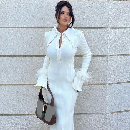 Frau in elegantem weißen Kleid mit Federn, hält braune Handtasche, steht vor heller Wand. Modetrend, Damenmode, stilvolles Outfit.